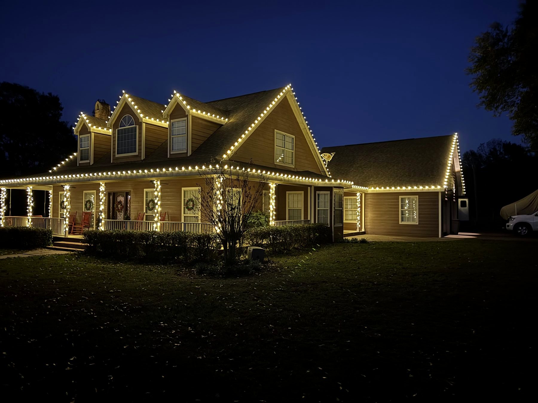 Farmhouse with warm-white roofline and wraparound porch lighting at dusk in Baldwin County
